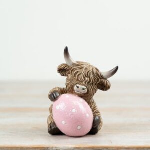 Highland cow ornament holding a sparkly pink Easter egg with white polka dots, detailed figurine for Easter and spring farmhouse decor.