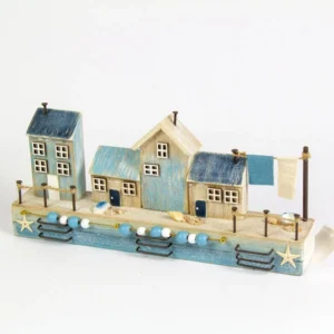 Wooden harbourside scene ornament featuring four coastal cottages in soft seaside colours, designed as a decorative nautical home décor display measuring 25cm wide.