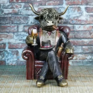 Highland cow ornament seated in an armchair wearing a suit and bow tie, holding a glass with a cigar, designed as a humorous rustic home decor figurine.