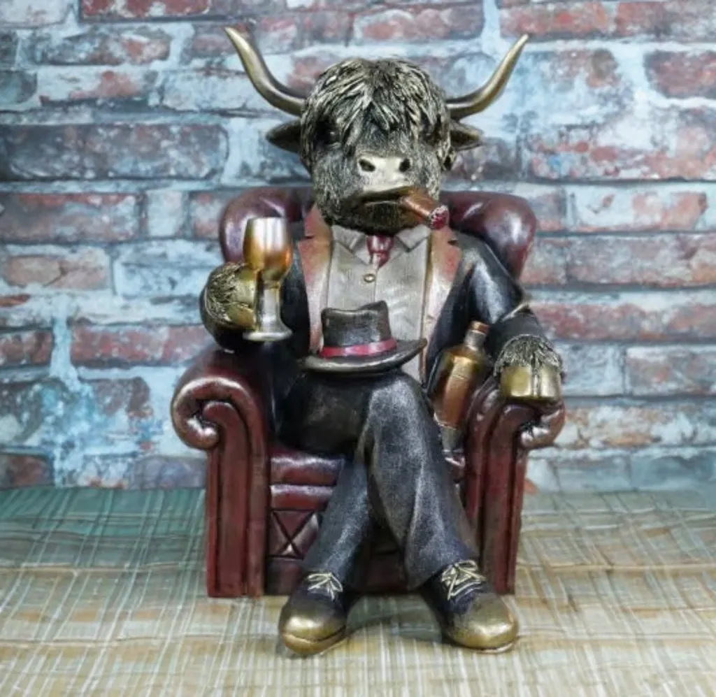Highland cow ornament seated in an armchair wearing a suit and bow tie, holding a glass with a cigar, designed as a humorous rustic home decor figurine.