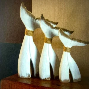 Set of three wooden whale tail ornaments in varying sizes with distressed white finish and rope detailing, styled as coastal nautical home décor.