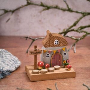 Toadstool Tales wooden acorn house decoration with an acorn-shaped roof, grey cottage, pink door, yellow bunting, red toadstools, flower details, and a Welcome sign on a wooden base.