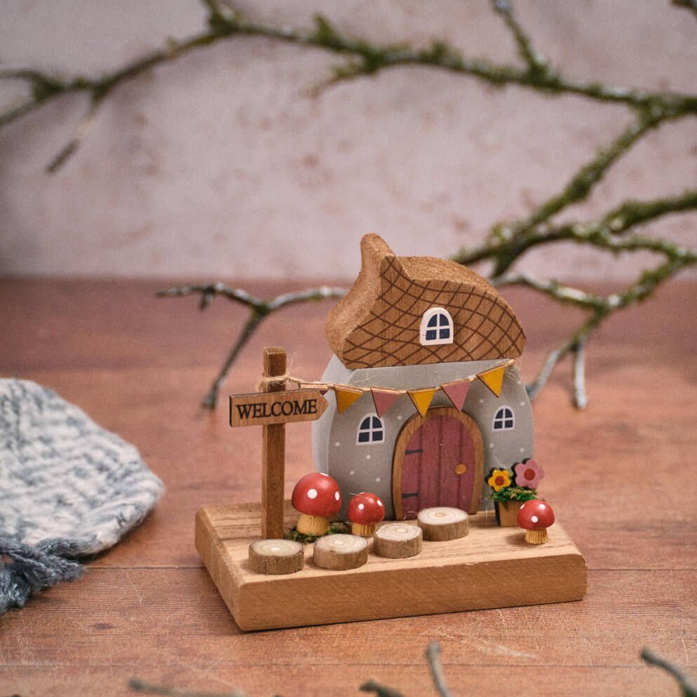 Toadstool Tales wooden acorn house decoration with an acorn-shaped roof, grey cottage, pink door, yellow bunting, red toadstools, flower details, and a Welcome sign on a wooden base.