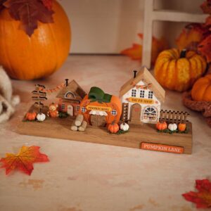 Harvest Home wooden Pumpkin Lane decoration featuring three painted houses labelled Harvest Hall, Pumpkin House, and The Pie Shop with miniature pumpkins, faux logs, greenery, and a Pumpkin Lane sign on a wooden base.