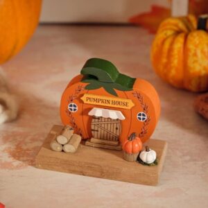 Decorative wooden Harvest Home pumpkin house ornament featuring an orange pumpkin-shaped house with green roof, miniature wood logs, orange and white pumpkins on a rectangular wooden base.